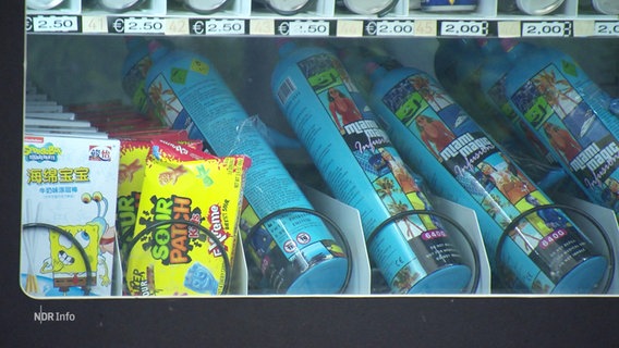 Kartuschen mit Lachgas liegen neben Süßigkeiten in einem Snack-Automaten. © Screenshot 