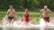 Drei DLRG Rettungsschwimmer, zwei Männer und eine Frau, rennen in einen Badesee. Rechts rennt der 76 jährige Klaus Kläre, in der Mitte eine Frau in rotem Badeanzug und mit roter Schwimmboje. Die Szene erinnert an die Serie Baywatch. © Screenshot 