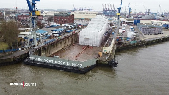 Eine eingerüstete Yacht steht auf einem Trockendock. © Screenshot 