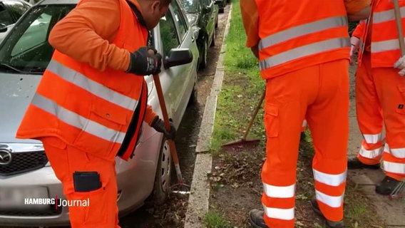 Mehrere Mitarbeitende der Stadtreinigung müssen einen Straßenabschnitt mühsam mit der Hand säubern, weil dort ein Auto geparkt ist. © Screenshot 