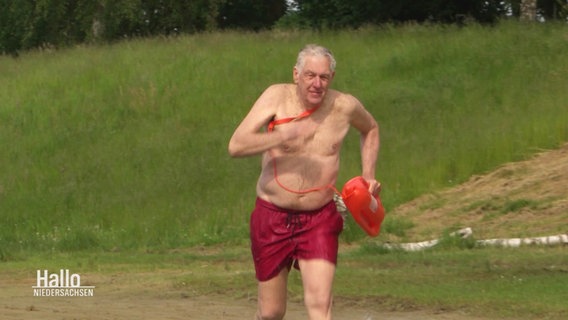 Der 76-jährige Rettungsschwimmer Klaus Kläres sprinted mit einer roten Rettungsboje in einen Badesee. © Screenshot 
