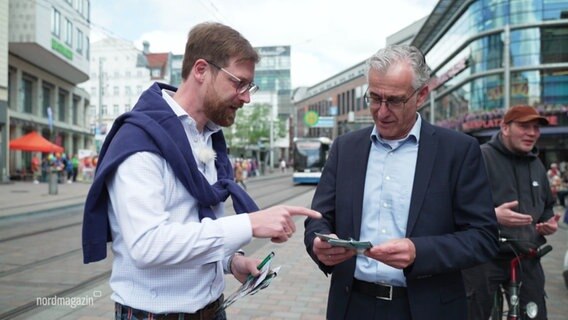 Joscha Dopp beim Wahlkampf: Er spricht mit einem älteren Mann im Anzug, dem er Wahlkampf-Flyer in die Hand gegeben hat. © Screenshot 