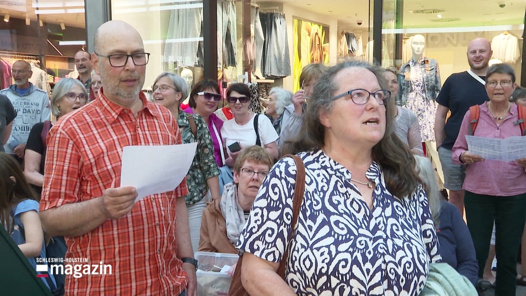 Eine Menschengruppe steht in einem Shopping Center und singt.