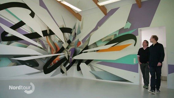 Der Kunstsammler Rik Reinking und der Künstler DAIM getreten einen Raum mit einem bunten Wandgemälde. © Screenshot 