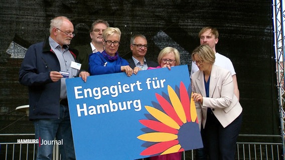 Hamburger Ehrenamtliche stehen auf einer Bühne und halten gemeinsam eine große blaue Tafel mit der Aufschrift "Engagiert für Hamburg". © Screenshot 