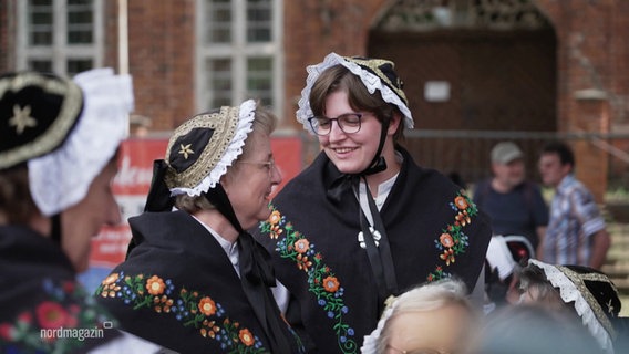 Zwei Frauen in traditionellen Trachten lächeln sich zu. © Screenshot 