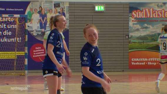 Zwei Handballerinnen in blauen Trikots stehen lächeln auf dem Feld. © Screenshot 