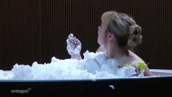 Eine blonde Frau mit Dutt sitzt in einer mit Schaum gefüllten Badewanne. © Screenshot 