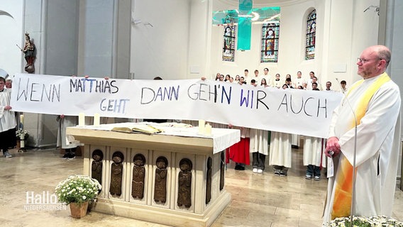 Gemeindemitglieder halten hinter dem Altar ein Banner hoch, um ihre Solidarität zu bekunden. © Screenshot 