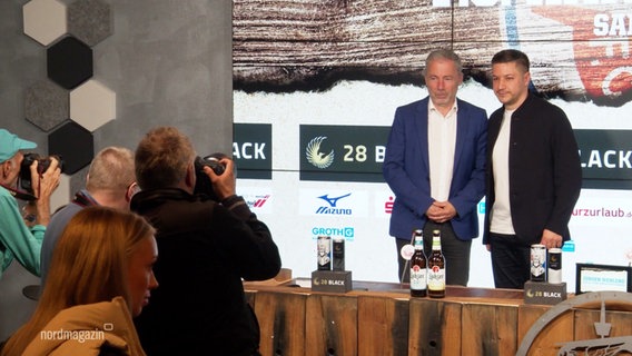 Jürgen Wehlend und Amir Shapourzadeh werden auf einer Pressekonferenz fotografiert. © Screenshot 