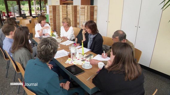 Mitarbeitende eines Wohlfahrtsverbandes beraten sich an einem Tisch. © Screenshot 