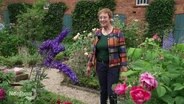 Eine Frau steht in einem Garten zwischen vielen Blumen. © Screenshot 