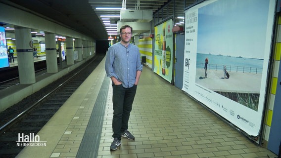 Ein Mann steht an einer U-Bahn Station vor einem dort plakatierten Foto. © Screenshot 