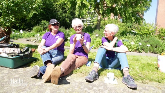 Drei ältere Frauen in lila T-Shirts sitzen gemeinsam in der Sonne. © Screenshot 