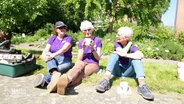 Drei ältere Frauen in lila T-Shirts sitzen gemeinsam in der Sonne. © Screenshot 