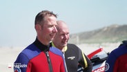 Rettungsschwimmer Hajo Götz Neumann im Neoprenanzug am Strand. © Screenshot 