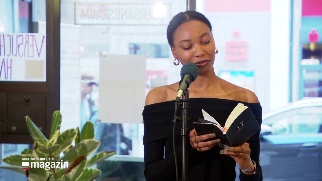 Eine junge schwarze Frau am Mikrofon bei einem Poetry Slam, sie liest aus einem Buch vor.