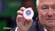 Ein Mann hält eine Scheibe mit dem Logo des Fußballvereins Holstein Kiel in die Kamera (Quelle: ARD Sportschau). © Screenshot 