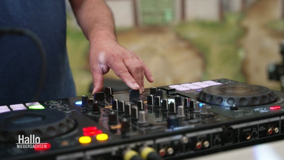 Ein DJ schiebt den Regler eines Mischpults nach oben. © Screenshot 