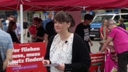 Marianne Esther steht vor einem Stand der Linken und verteilt Flyer in der Innenstadt. © Screenshot 