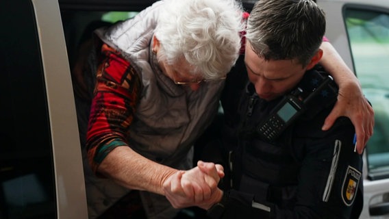 Ein Polizist stützt eine alte Frau, die einen Arm um seine Schultern gelegt hat. © Screenshot 