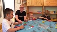 Kita-Chefin Nancy Wullf sitzt mit Kindern am Tisch. © Screenshot 