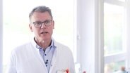 Olav Kraufse von der Diakovere Henriettenstift Hannover im Interview. Er trägt kurze graue Haare, eine Brille und einen weißen Arztkittel. © Screenshot 