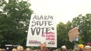 Über den Köpfen eines draußen feiernden Konzertpublikums wird ein Plakat hochgehalten auf dem steht: "Alarmstufe Vote". © Screenshot 