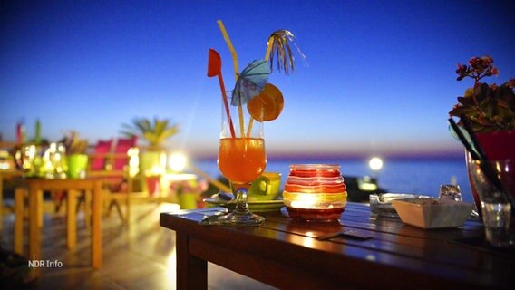 Ein Cocktail auf einem Tisch bei Sonnenuntergang. © Screenshot 