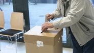 Jemand schmeißt einen Stimmzettel in eine Wahlurne. © Screenshot 