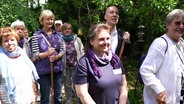 Frauen und Männer verschiedenen Alters stehen mit Harken und Schaufeln in ihrem Gemeinschaftsgarten. © Screenshot 