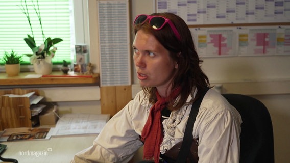 Lydia Fischer sitzt in einem Büro. Sie trägt Piratenkleidung und hat eine pinke Sonnenbrille zurückgeschoben auf dem Kopf. © Screenshot 