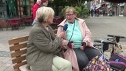 Susanne Stichler sitzt auf eineer Bank und interviewt eine Dame, die neben ihr sitzt. © Screenshot 