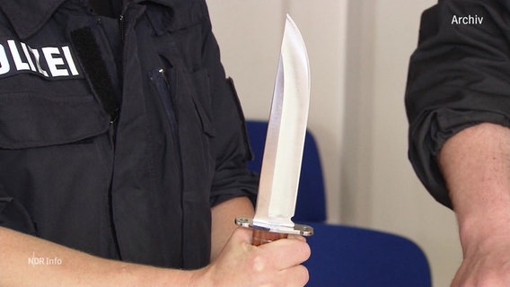 Ein Polizeibeamter hält ein großes Messer. (Archivfoto) © Screenshot 