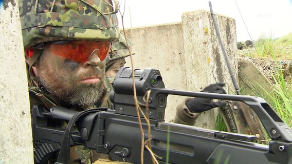 Ein Bundeswehrsoldat mit Gewehr und Schutzausrüstung in Tarnfarben bei einer Geländeübung © Screenshot 