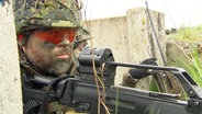 Ein Bundeswehrsoldat mit Gewehr und Schutzausrüstung in Tarnfarben bei einer Geländeübung © Screenshot 