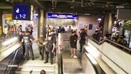 Blick aus der Ferne auf einen Bahnhof. Treppen und Rolltreppen führen runter zu den Gleisen. Überall steht Polizei mit schwarzer Schutzausrüstung. © Screenshot 