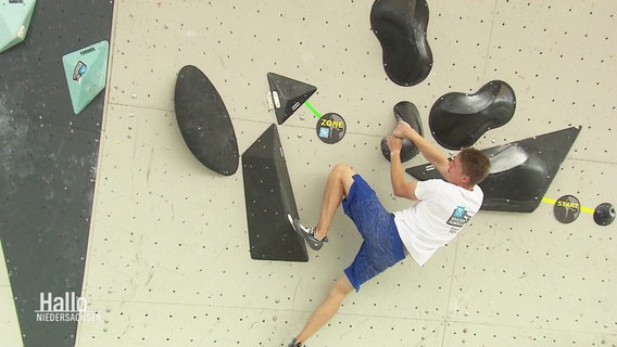 Ein Sportler zieht sich an einer Boulderwand hoch. © Screenshot 