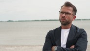 Tourismuschef Knut Schäfer steht mit verschränkten Armen an einem Ufer. © Screenshot 