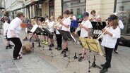 Kinder in weißen Hemden spielen auf ihren Blechblasinstrumenten - davor ihre Dirigentin. © Screenshot 