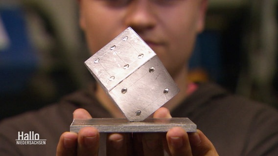 Eine Person hält einen Würfel aus Metall in die Kamera. © Screenshot 