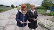 Zwei Frauen vergleichen Archivfotos einer Straße mit dem Bild von heute. © Screenshot 