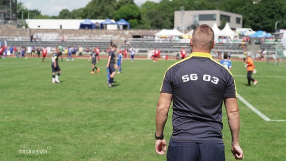 Am Mann im Fußball-Trikot steht am Rande eines Spielfeldes. © Screenshot 