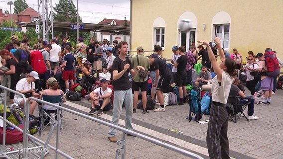 Wartende (und ballspielende) Fusion-Besucher:innen bei der Abreise an einem Bahnhof. © Screenshot 