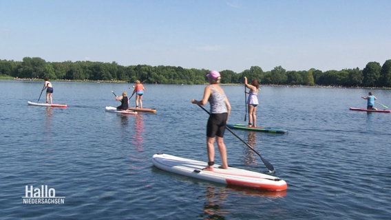 Teilnehmerinnen eines Kurses der Landfrauen paddeln mit Stand-Up-Booten auf einem See. © Screenshot 
