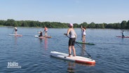 Teilnehmerinnen eines Kurses der Landfrauen paddeln mit Stand-Up-Booten auf einem See. © Screenshot 