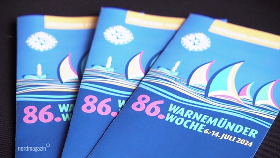 Werbesprospekte der Warnemünder Woche liegen auf einem Tisch. © Screenshot 