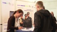 Zwei Jugendliche lassen sich etwas von einer Frau am Polizei-Stand erklären. © Screenshot 