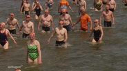 Menschen in Badekleidung waten durch seichtes Gewässer. © Screenshot 