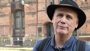 Denkmalschützer Albert Schett im Interview. Er ist ein Mann jenseits der 60. Er trägt einen schwarzen Hut und schaut offen in die Kamera. © Screenshot 